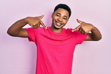 Young african american man wearing casua t shirt looking confident with smile on face, pointing...