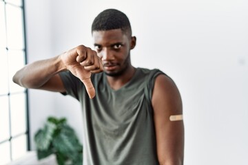 Young african american man getting vaccine showing arm with band aid with angry face, negative sign...