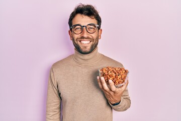 Handsome man with beard holding peanuts looking positive and happy standing and smiling with a confident smile showing teeth