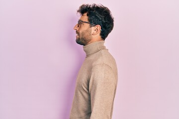 Handsome man with beard wearing turtleneck sweater and glasses looking to side, relax profile pose...