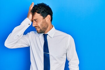 Handsome man with beard wearing business shirt and tie surprised with hand on head for mistake,...