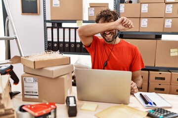 Young hispanic call center agent man working at warehouse smiling cheerful playing peek a boo with...