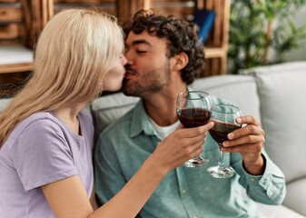 Young couple kissing and toasting with red wine glass at home.