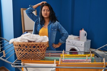 Young asian woman hanging clothes at clothesline confuse and wonder about question. uncertain with doubt, thinking with hand on head. pensive concept.