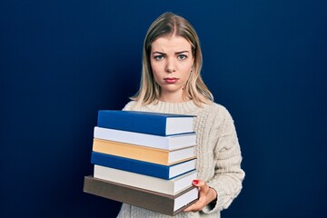 Beautiful caucasian woman holding a pile of books skeptic and nervous, frowning upset because of problem. negative person.