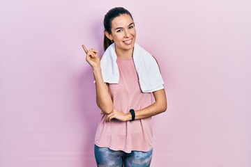 Young brunette woman wearing sportswear and towel with a big smile on face, pointing with hand and finger to the side looking at the camera.