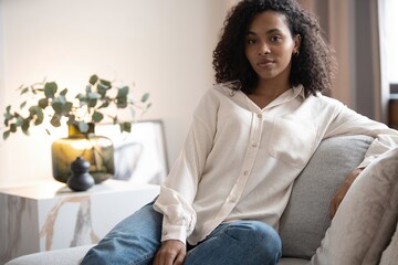 Portrait of lovely young mixed race woman smiling and looking at camera, sitting on sofa at home