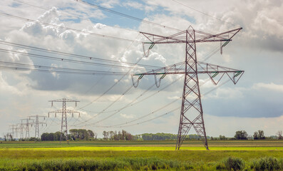 Power lines and pylons in a rural area. The photo was taken in the Dutch province of North Brabant on a cloudy day in the spring season.