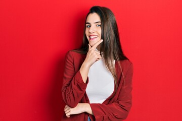 Young brunette teenager wearing business jacket looking confident at the camera smiling with crossed arms and hand raised on chin. thinking positive.