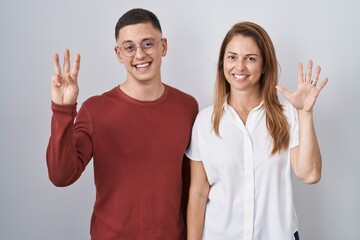 Mother and son standing together over isolated background showing and pointing up with fingers number eight while smiling confident and happy.