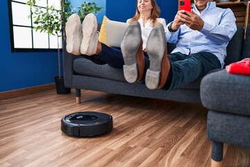 Middle age man and woman couple cleaning floor using robot cleaner at home