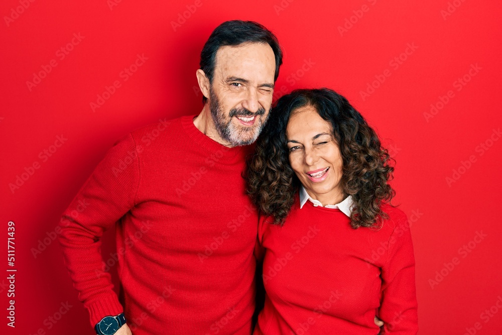 Sticker Middle age couple of hispanic woman and man hugging and standing together winking looking at the camera with sexy expression, cheerful and happy face.