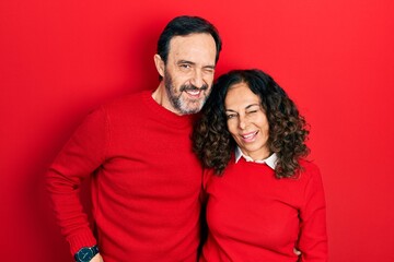 Middle age couple of hispanic woman and man hugging and standing together winking looking at the...