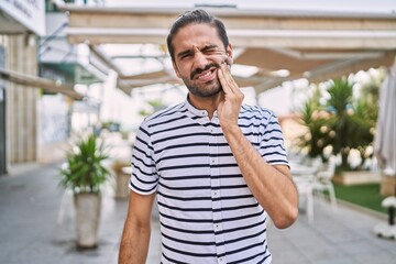 Young hispanic man with beard outdoors at the city touching mouth with hand with painful expression because of toothache or dental illness on teeth. dentist