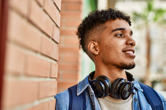 Hispanic young man smiling wearing headphones leaning on bricks wall