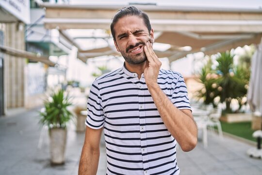 Young hispanic man with beard outdoors at the city touching mouth with hand with painful expression because of toothache or dental illness on teeth. dentist - Powered by Adobe