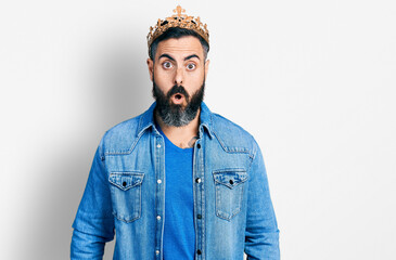 Hispanic man with beard wearing king crown scared and amazed with open mouth for surprise,...