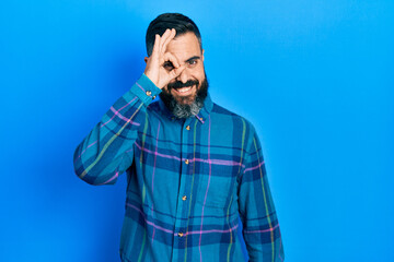 Young hispanic man wearing casual clothes doing ok gesture with hand smiling, eye looking through fingers with happy face.