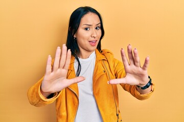 Beautiful hispanic woman with nose piercing wearing yellow leather jacket doing stop gesture with hands palms, angry and frustration expression