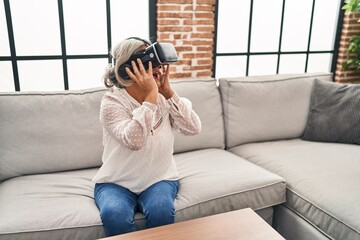 Middle age woman playing video game using virtual reality glasses at home