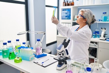 Fototapeta na wymiar Middle age woman wearing scientist uniform looking test tubes at laboratory