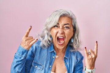 Middle age woman with grey hair standing over pink background shouting with crazy expression doing...