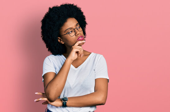 Young african american woman wearing casual white t shirt with hand on chin thinking about question, pensive expression. smiling with thoughtful face. doubt concept.