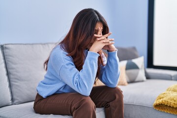 Young hispanic woman stressed sitting on sofa at home