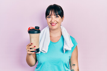 Young hispanic woman wearing sport clothes drinking a protein shake looking positive and happy...
