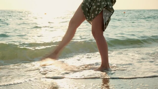 Woman legs in the sea water. Carefree girl barefoot enjoys summer at the beach, jumping at seaside. Travel, vacation concept.