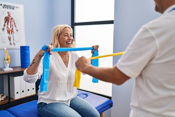 Middle age man and woman physiotherapist and patient having rehab session using elastic band at...