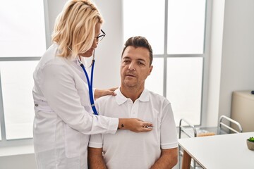 Middle age man and woman doctor and patient ausculateting heart having medical consultation at clinic