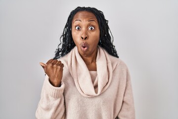 African woman standing over white background surprised pointing with hand finger to the side, open mouth amazed expression.