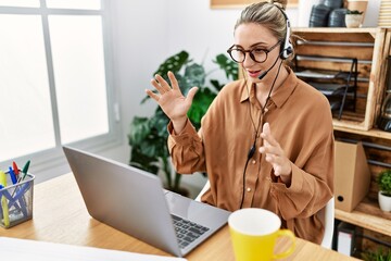 Young blonde woman wearing call center agent headset having video call at office