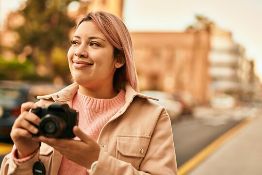Young hispanic girl smiling happy using reflex camera at the city.