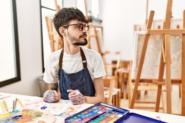 Hispanic man with beard at art studio looking to side, relax profile pose with natural face with confident smile.