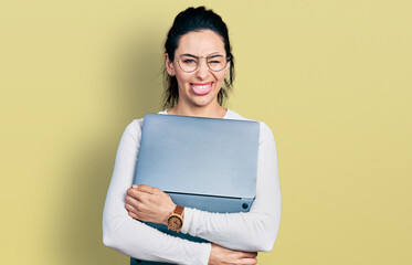 Young hispanic woman working using computer laptop sticking tongue out happy with funny expression.