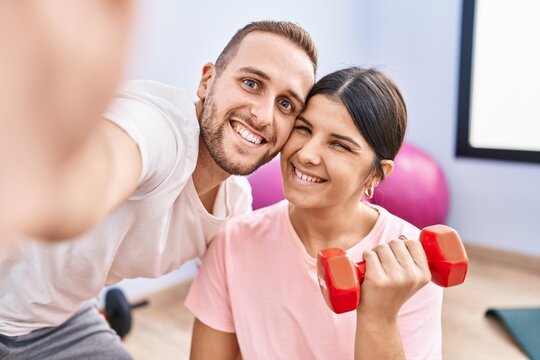 Man and woman couple training using dumbbells make selfie by the camera at sport center