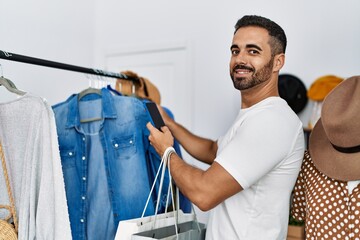 Young hispanic man customer choosing clothes make photo to shirt at clothing store