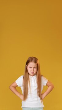 Dissatisfied child. Warning gesture. Discipline punishment. Vertical portrait of angry annoyed disturbed girl in white finger wagging shaking fist isolated on orange copy space background.