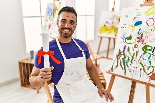 Young hispanic man smiling confident holding diploma at art studio
