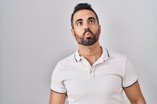 Young hispanic man with beard wearing casual clothes over white background making fish face with lips, crazy and comical gesture. funny expression.
