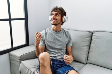 Young hispanic man listening to music playing air guitar gesture at home
