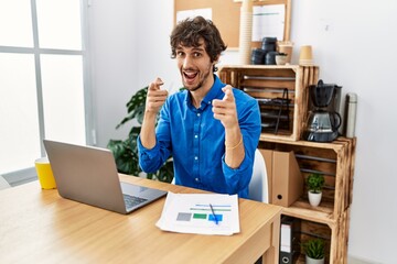 Young hispanic man with beard working at the office using computer laptop pointing fingers to camera with happy and funny face. good energy and vibes.