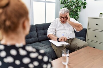 Senior psychologist man at consultation office looking at the watch time worried, afraid of getting...
