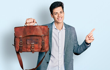 Young hispanic man holding business bag smiling happy pointing with hand and finger to the side