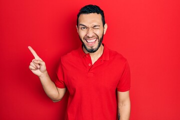 Hispanic man with beard pointing with fingers to the side winking looking at the camera with sexy...