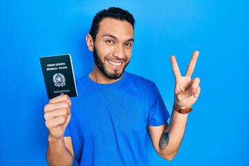 Hispanic man with beard holding italy passport smiling looking to the camera showing fingers doing...
