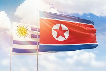 Sunny blue sky and flags of north korea and uruguay