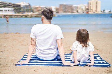 Father and daughter sitting on sand together at beach
